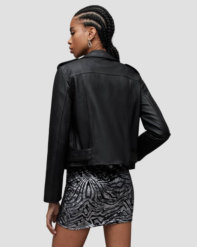 Person wearing a black leather jacket and patterned skirt on a plain background