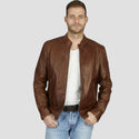 Man wearing a brown leather jacket over a white shirt and blue jeans on a light gray background