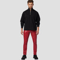 Man wearing a black half-zip sweater and red pants on a light gray background