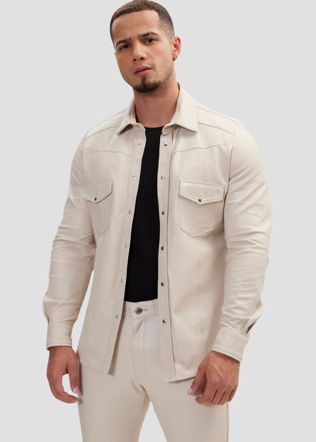 Man wearing a beige shirt over a black t-shirt with light-colored pants on a plain background