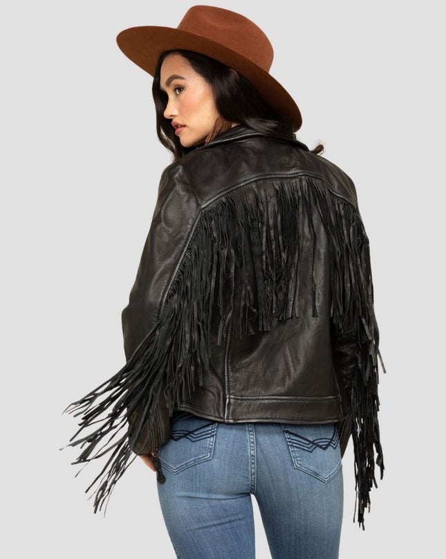 Woman wearing a black fringe leather jacket and brown hat on a gray background